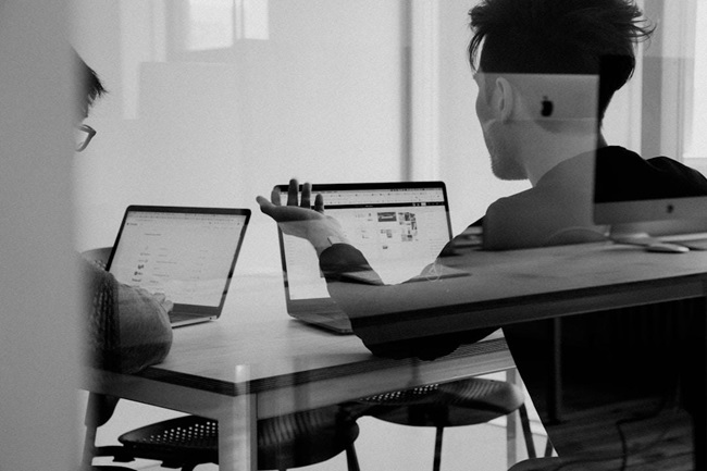 Two people collaborating at a table with laptops, focused on proposal automation tasks.