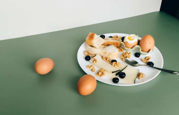 Plate of cheese, boiled eggs, bread, walnuts, and blueberries for a hearty breakfast.
