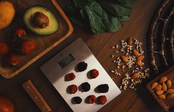 Top view of composed raw almond with seeds and avocado on table with berries on scales for cooking healthy dish