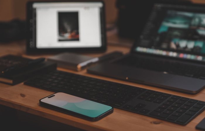 A contemporary workspace setup featuring a laptop, smartphone, and tablet on a wooden desk.