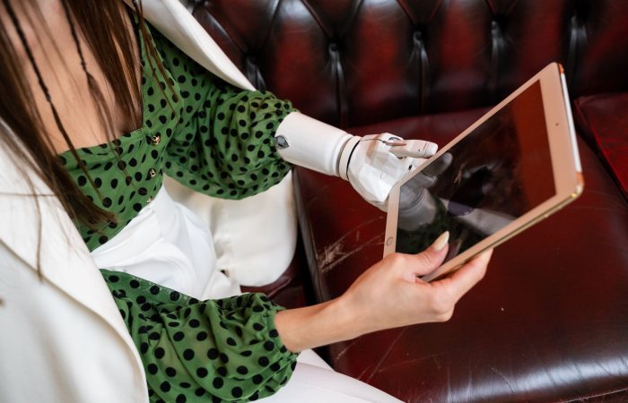 A woman using her prosthetic hand to interact with a digital tablet indoors, highlighting technology and accessibility.