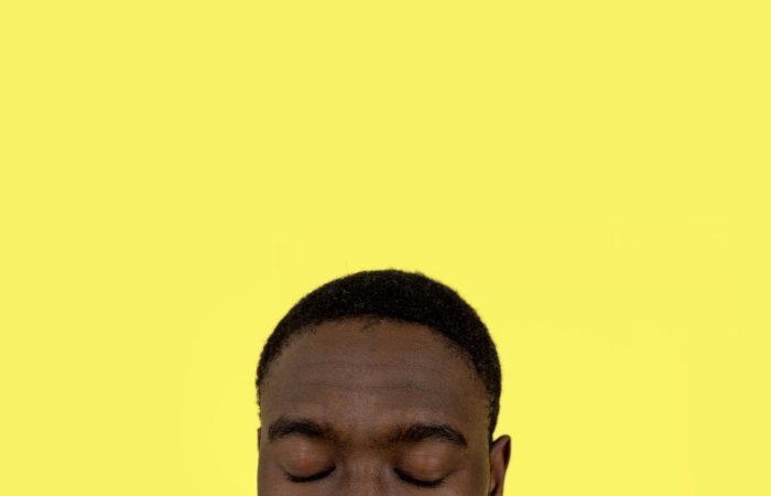 Close-up portrait of a man with eyes closed against a yellow background, evoking calmness and introspection.