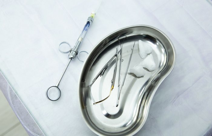 A set of sterile medical tools and syringe displayed in a kidney tray for dental or surgical use.