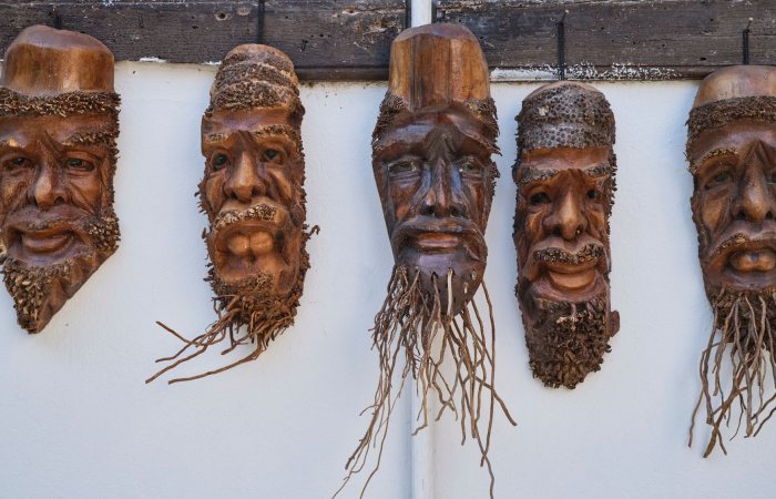 A set of handmade carved wooden tribal masks hanging on a wall.