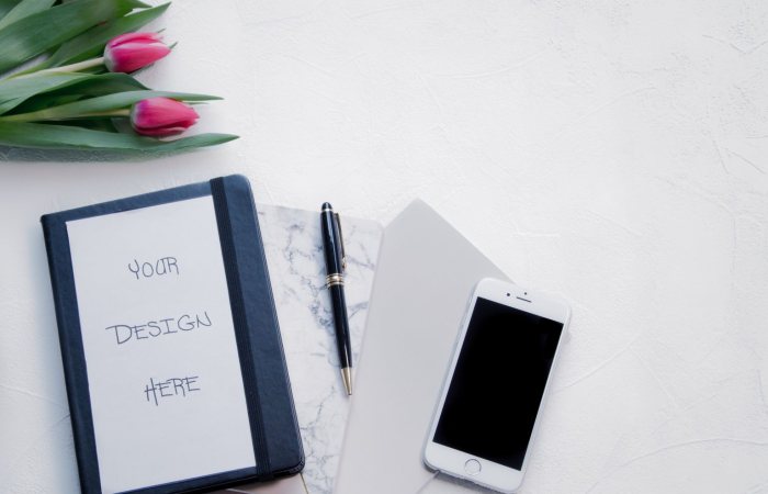 Flat lay of a workspace with tulips, a notebook, pen, and smartphone, perfect for designs.