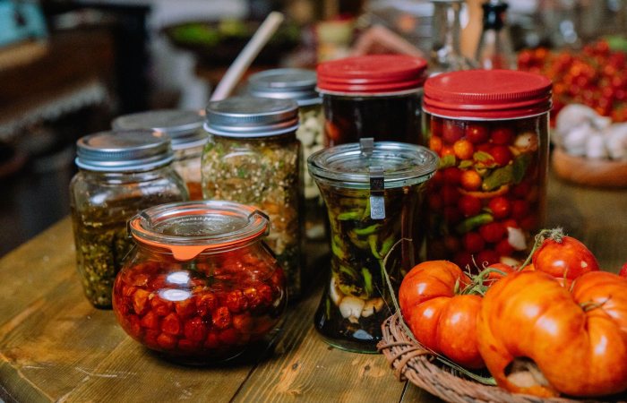 Colorful jars of homemade preserved vegetables and pickles on a rustic wooden table.