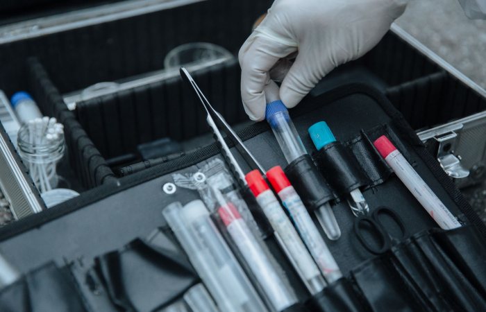 Gloved hand handling test tube in forensic equipment case at crime scene.