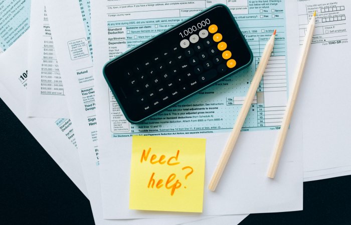 Top view of financial papers with a calculator, pencils, and a note saying 'Need help?' indicating tax or accounting assistance.
